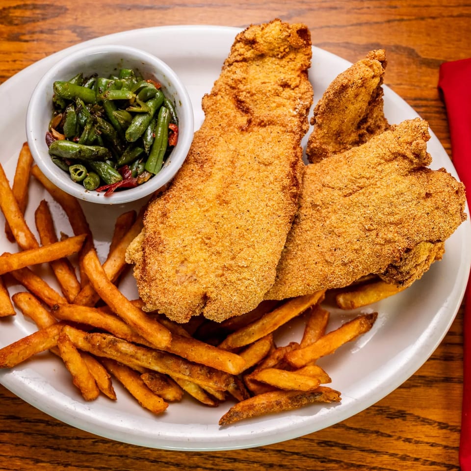 Fried fish fillets with french fries and a side of green beans on a white plate.