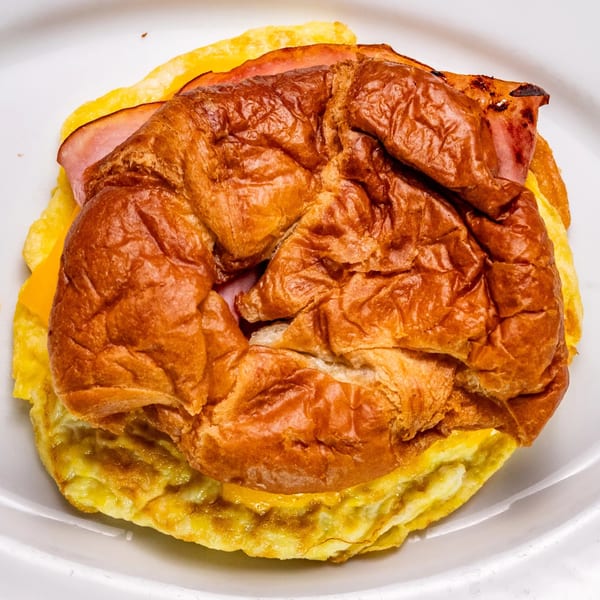 A close-up of a breakfast sandwich with ham, cheese, and egg on a brioche bun.