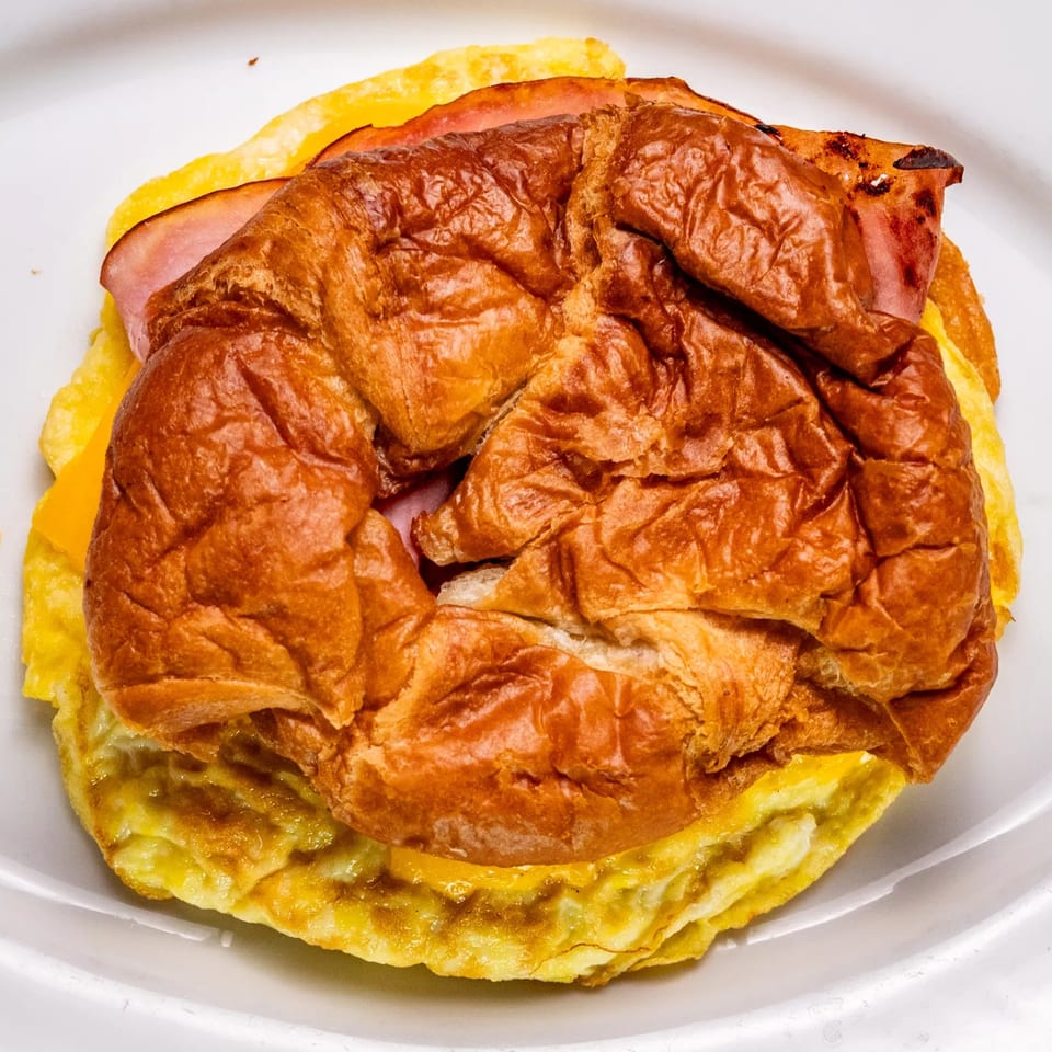 A close-up of a breakfast sandwich with ham, cheese, and egg on a brioche bun.