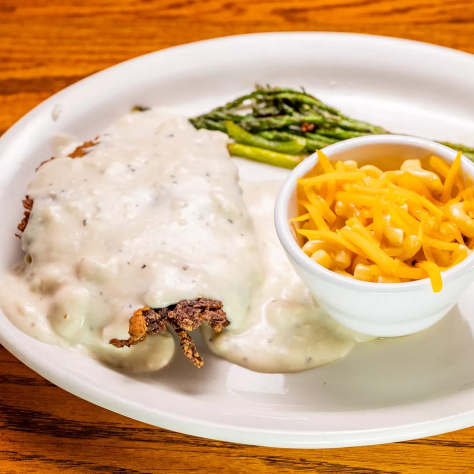 Chicken fried steak with gravy, a side of asparagus, and a bowl of mac and cheese.